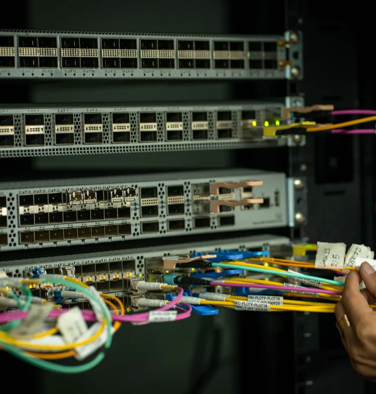 Hand steckt Glasfaserkabel in einem Serverschrank
